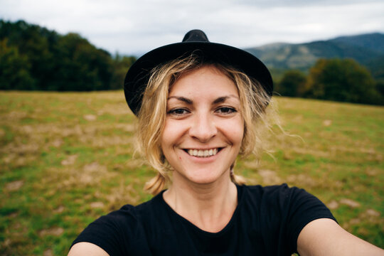 young blonde girl takes a selfie in a black hat and t-shirt