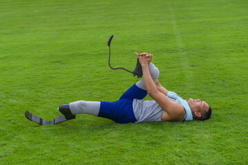 Asian athlete with prosthetics stretches on grass lawn, concluding his speed running practice at the stadium