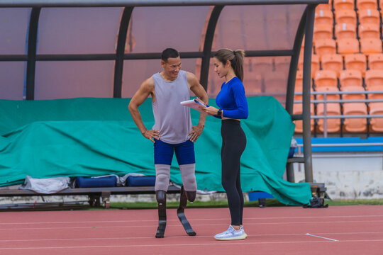 Male athlete with prosthetic blades, alongside female trainer, outlining the day's speed running training at the sports stadium