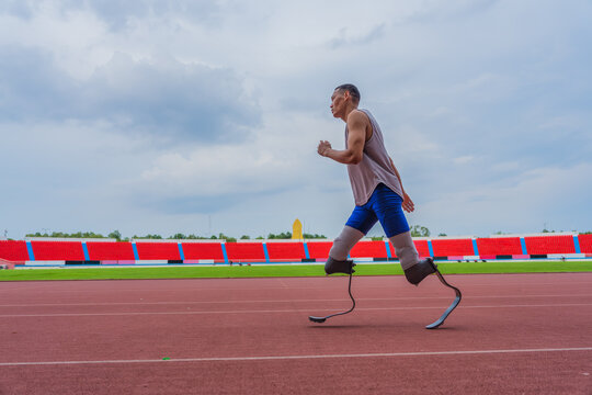 Dedicated Asian speed runner, equipped with two prosthetic running blades, jogging steadily on the running track at the local sports stadium