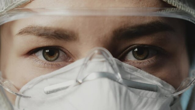 Stay safe. Close up of eyes of young female doctor wearing medical mask looking at camera isolated over white background. Healthcare and medicine concept. Selective focus on one eye. Slow motion