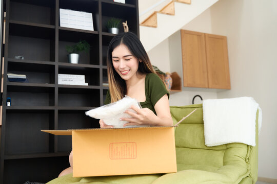 Young asian women unpacking awaited parce looking inside, sitting at sofa, unhappy customer opening cardboard box with online store order,Delivery service concept.