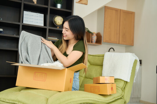 Young asian women unpacking awaited parce looking inside, sitting at sofa, unhappy customer opening cardboard box with online store order,Delivery service concept.