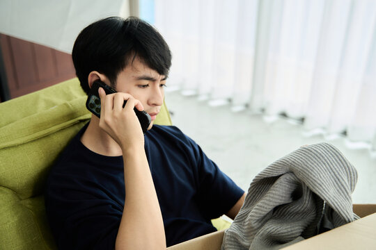 Young asian man unpacking awaited parce looking inside, sitting at sofa, unsatisfied customer opening cardboard box with online store order ,Delivery service concept.