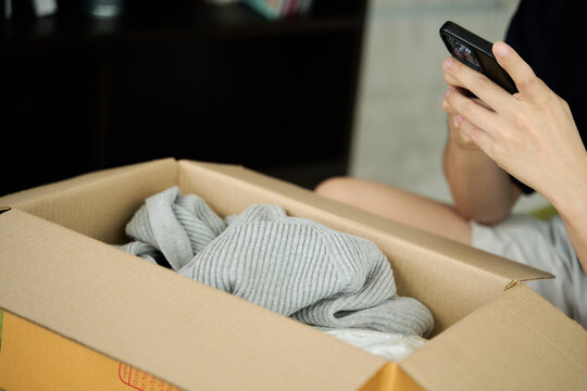 Young asian man unpacking  awaited parce looking inside, sitting at sofa, satisfied happy customer opening cardboard box with online store order, good shipping delivery service