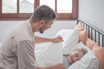 Father singing his daughter to sleep, providing comfort, support, and security. Focusing on fulfilling both physical and emotional needs. Kids sometimes act happy while pretending to fall asleep.