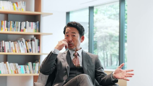 Middle-aged Asian businessman talking to camera. Interview video.
