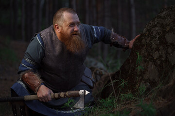 Lurking medieval red-haired viking warrior with beard with an ax in forest - 615289934