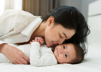 mother kissing her infant baby on bed