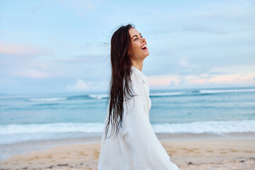 Fototapeta na wymiar Brunette woman with long hair in a white shirt and jean shorts tan and happy running on the beach and having fun smile with teeth in front of the ocean, vacation summer trip