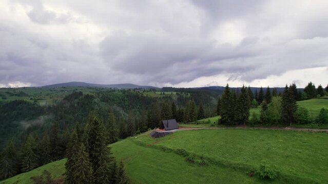 Aerial view of a remote A frame cabin in a evergreen forest, alpine background