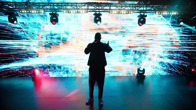 African-American Black rap artist performing his gig in front of a concert crowd on a stage of a large venue, surrounded by bright flashig lights