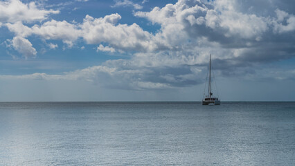 A lonely yacht in a calm turquoise ocean. A tall mast against a background of blue sky and clouds. Seychelles.