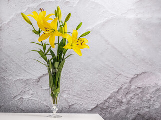 Bouquet of yellow lilies in a glass vase on a white table.