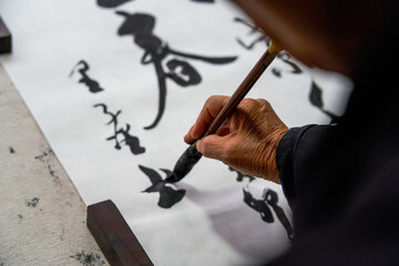 An old Chinese calligrapher is writing brush characters, creating Chinese calligraphy works.
Translation: Spring comes, the god of wind arrives. - obrazy, fototapety, plakaty