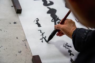 An old Chinese calligrapher is writing brush characters, creating Chinese calligraphy...