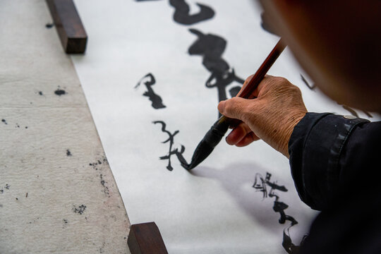 An old Chinese calligrapher is writing brush characters, creating Chinese calligraphy works.
Translation: Spring comes, the god of wind arrives.