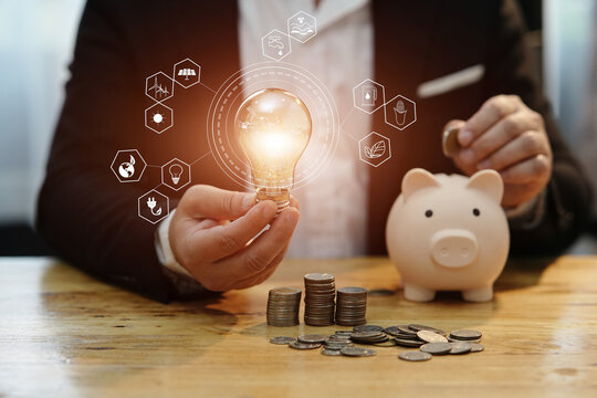 Businessman holding a light bulb Concept of saving money with hands putting coins on wooden table floor