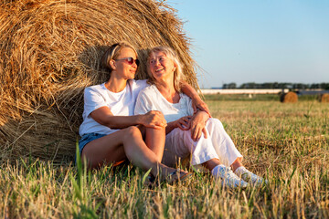 Women in the field with hay rolls. An elderly mother with an adult daughter in white clothes enjoy...