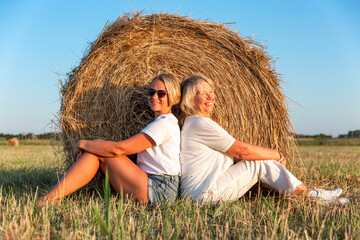 Naklejka na ściany i meble Women in the field with hay rolls. An elderly mother with an adult daughter in white clothes enjoy nature at sunset.