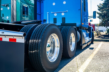 Blue big rig semi truck tractor with new wheels tires on alloy rims standing on the truck stop parking lot beside with another semi trucks