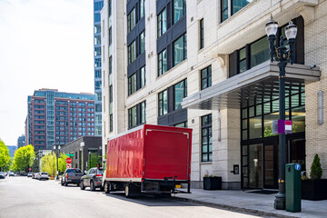 Compact small rig semi truck with red box trailer making customer delivery standing on the urban city street with multilevel apartment buildings
