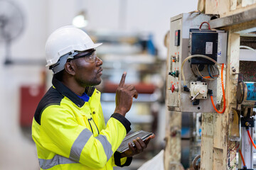 American male engineers in helmets and vests conduct close-up inspections of circuit boards at the...