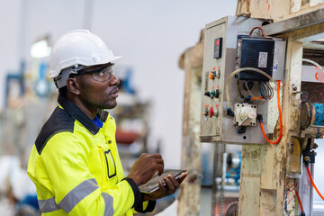 Wearing a helmet and vest, the American male engineer conducts a close-up inspection of the circuit...