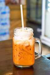 delicious thai iced tea with milk foam in a glass cup on a wooden table. Traditional Thai drink.