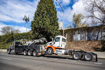 Powerful black big rig tow semi truck towing broken big rig semi truck without semi trailer driving...