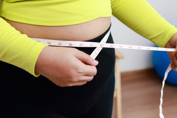 Fat Asian woman exercising at home using meter tape. Measuring waist circumference. Sports concept, health care. weight loss