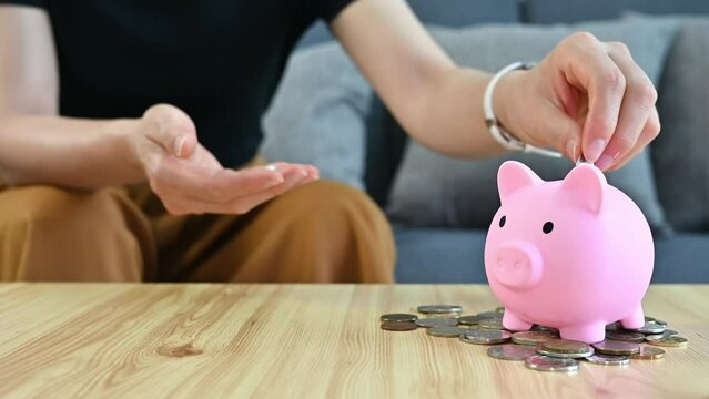 Woman while putting a coin into piggy bank for saving money.