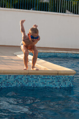 a little boy having fun jumping in a swimming pool wearing swimwear and googles.