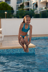 Naklejka premium A cute girl with blue swimsuit jumps in a swimming pool with big emotions , joy and fun.