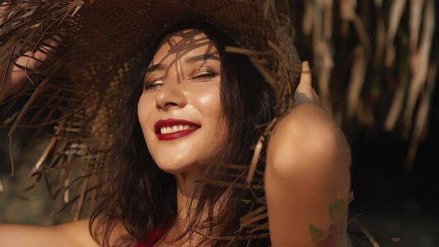 Young beautiful mixed race woman with a straw hat and in red dress in the hot summer day during vacation. Pretty asian girl smiling portrait. Beauty, travel, holidays, fashion concept and lifestyle.