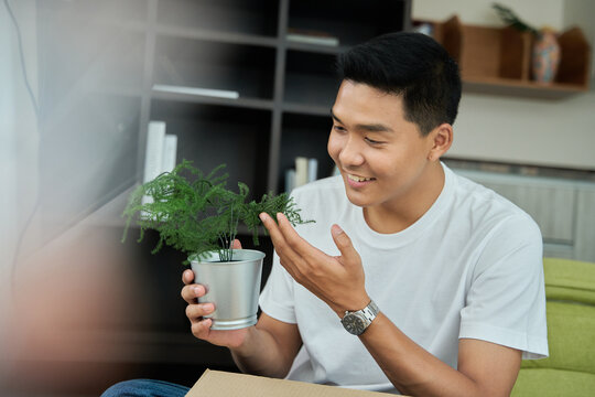 Young asian man unpacking  awaited parce looking inside, sitting at sofa, satisfied happy customer opening cardboard box with online store order, good shipping delivery service