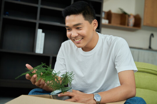 Young asian man unpacking  awaited parce looking inside, sitting at sofa, satisfied happy customer opening cardboard box with online store order, good shipping delivery service