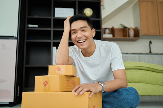 Young asian man unpacking  awaited parce looking inside, sitting at sofa, satisfied happy customer opening cardboard box with online store order, good shipping delivery service