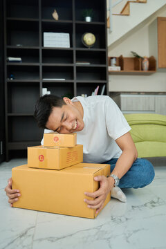 Young asian man unpacking  awaited parce looking inside, sitting at sofa, satisfied happy customer opening cardboard box with online store order, good shipping delivery service