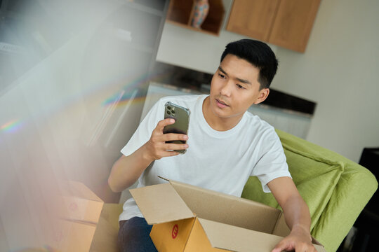 Young asian man unpacking awaited parce looking inside, sitting at sofa, unsatisfied customer opening cardboard box with online store order ,Delivery service concept.