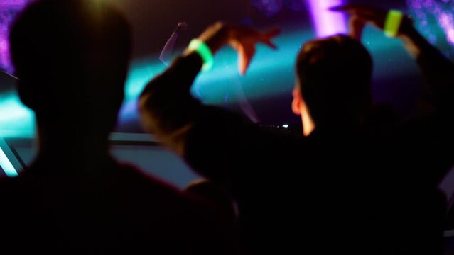 Portrait of attractive female techno DJ performing playing her music set on a stage in front of crowd in a nightclub during a festival, bright flashing stage lights, huge LED screen behind talent