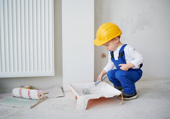 Little boy construction worker crouching down and preparing paint roller for wall painting. Kid...