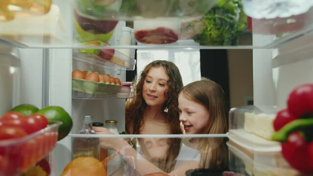 Woman and Girl Opening Fridge Door with Healthy Food and Taking Products. Happy Family Cooking Meal and Choosing Ingredients of Refrigerator. Life of Smiling People Selecting Storing Grocery to Eat