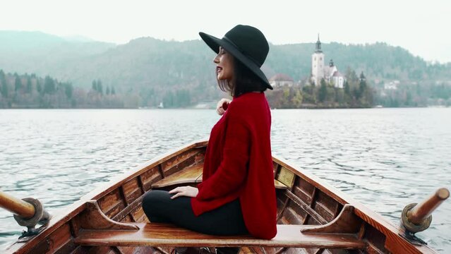 Happy asian woman turned back relaxing in boat on the beautiful summer lake during her vacation. Pretty young girl sitting in boat and looking for the inspiration at background of the Alph mountain.