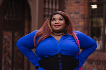 A beautiful woman takes a deep breath and smiles, looking up to the sky. She wears a pink purse, an ultramarine dress, and bright lipstick. Adding backstory, she is African American and college-age.