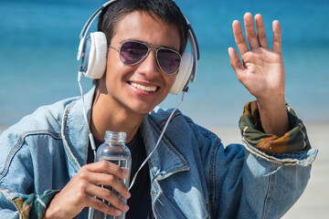 teenager with headphones drinking water relaxed on the beach and waving