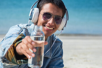 young man with headphones and bottle of water on the beach