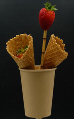 Disposable paper cup with a drinking straw. Edible wafer cups or cones. Strawberries.