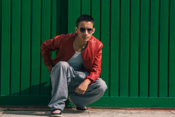 urban young man squatting posing on green wall