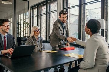 Smiling businessman shaking hand with new client in a modern office - obrazy, fototapety, plakaty